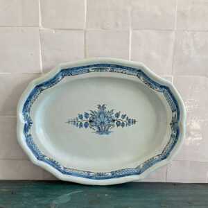 Plat en faïence dit cul noir, décor bleu panier fleuri stylisé, époque 1840-1870. Authentique faïence française du XIXᵉ siècle. Sa forme ovale à bord contourné et son décor bleu cobalt au panier fleuri rappellent les faïences traditionnelles du Nord-Ouest de la France, inspirées du style de Moustiers