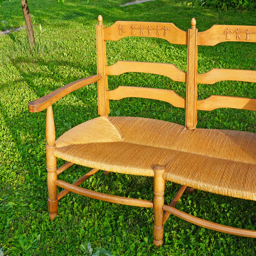 Détail du Radassier ou banquette provençale à 3 places, en bois massif avec assise paillée traditionnelle avec dossier sculpté d'une farandole d’Arlésiennes et de gardians pour les amateurs de Provence, de Camargue et d'Arles conjugués