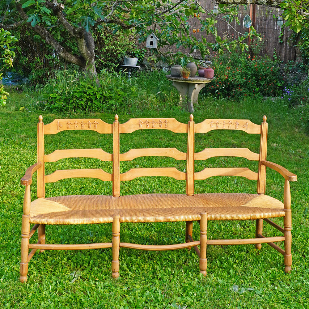 Radassier ou banquette provençale à 3 places, en bois massif avec assise paillée traditionnelle avec dossier sculpté d'une farandole d’Arlésiennes et de gardians pour les amateurs de Provence, de Camargue et d'Arles conjugués